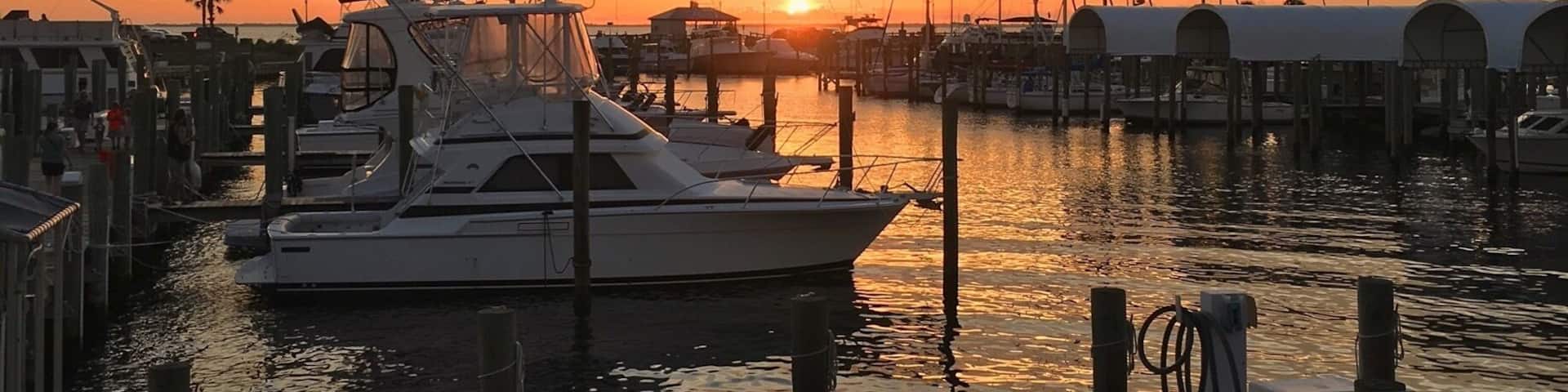 A marina at sunset with boats docked and a wooden pier.
