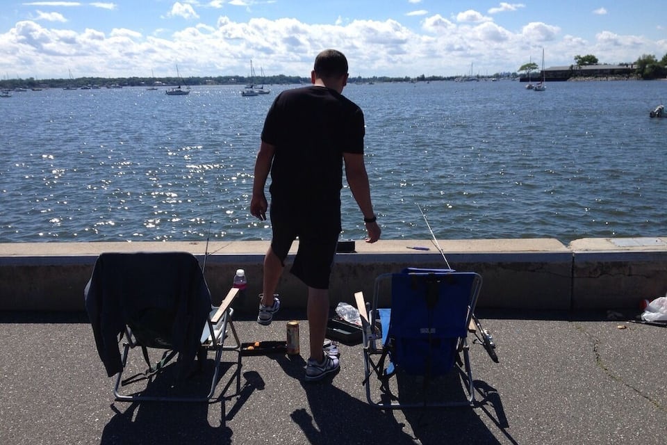A man fishing by the water with chairs and a can of soda nearby.