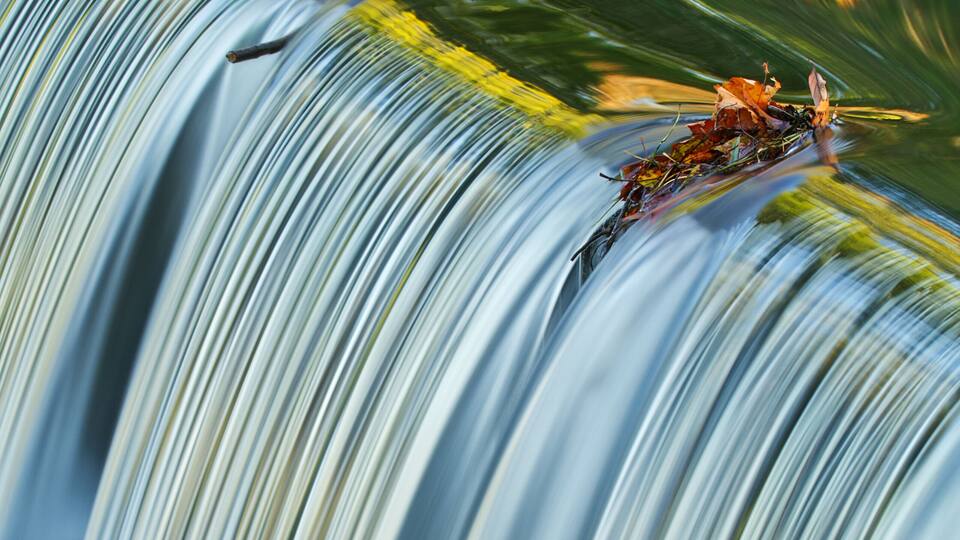 A waterfall with smooth water flow and autumn leaves on the rocks.