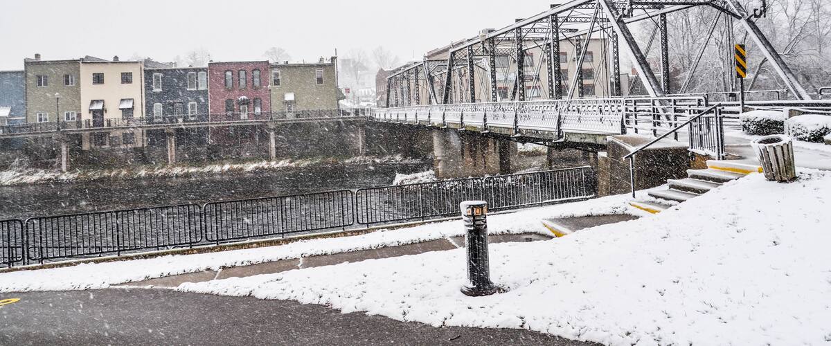 A snow-covered bridge with metal railings and a river below.