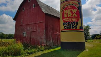 A red barn and a large cylindrical sign advertising 'The New Era Scientifically Processed Potato Chips'.