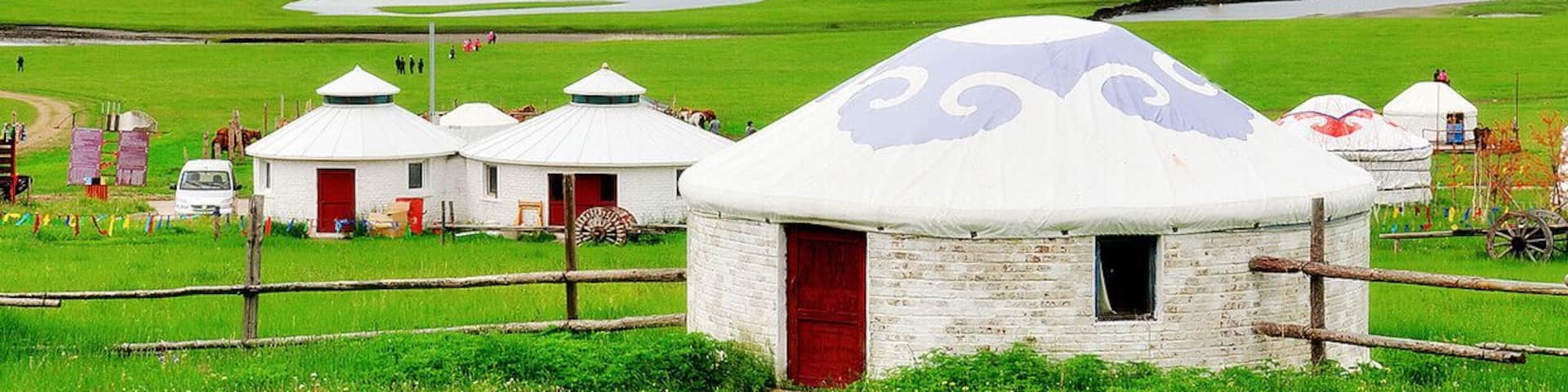A landscape with yurts, a green field, and distant mountains.