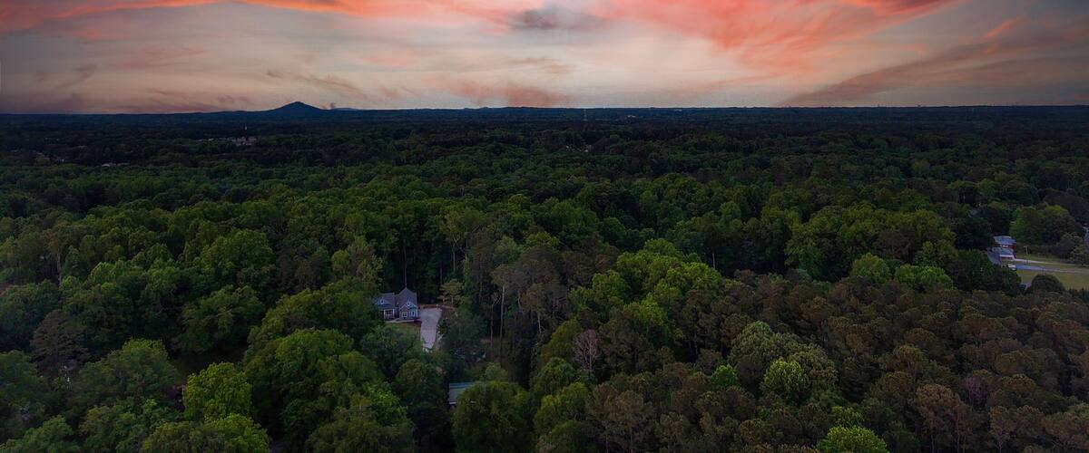 a breathtaking aerial panoramic shot of a sunset over Powder Springs Georgia with miles of vast green trees and homes with powerful clouds