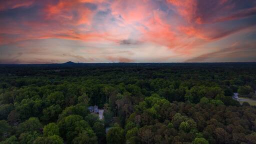 a breathtaking aerial panoramic shot of a sunset over Powder Springs Georgia with miles of vast green trees and homes with powerful clouds