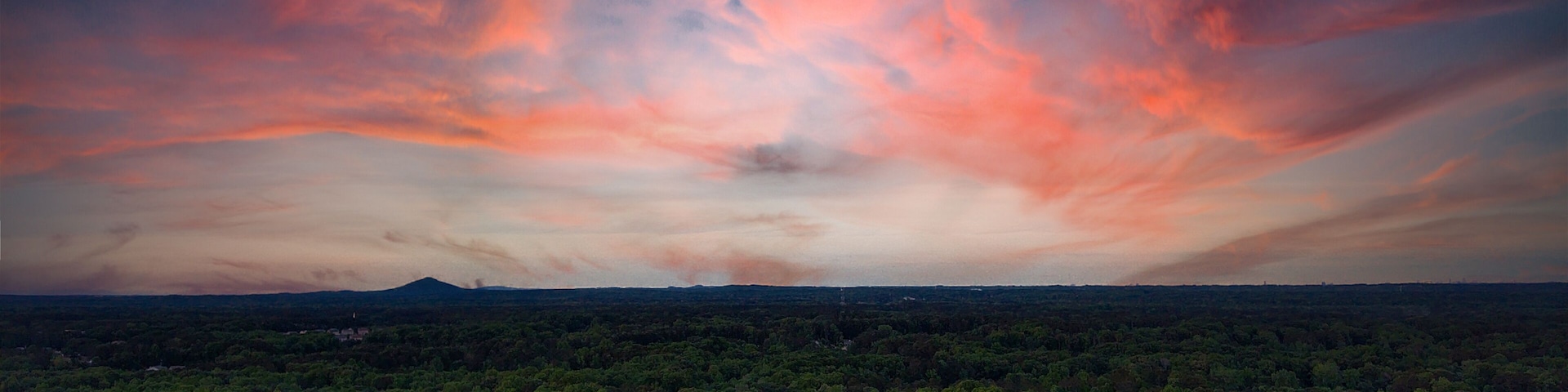 a breathtaking aerial panoramic shot of a sunset over Powder Springs Georgia with miles of vast green trees and homes with powerful clouds