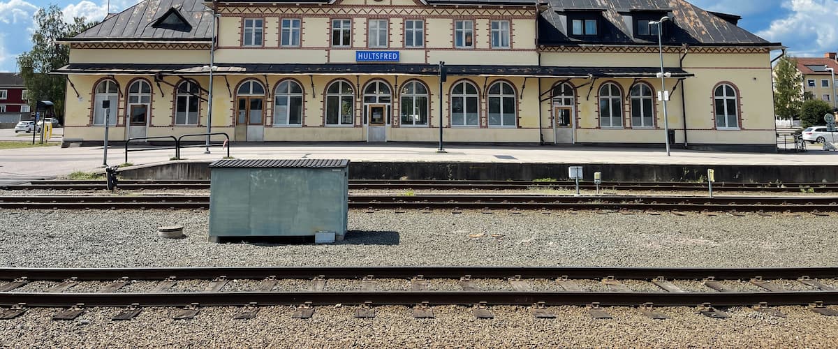 A train station with a clock tower, multiple tracks, and a sign reading "HULTSFRED".