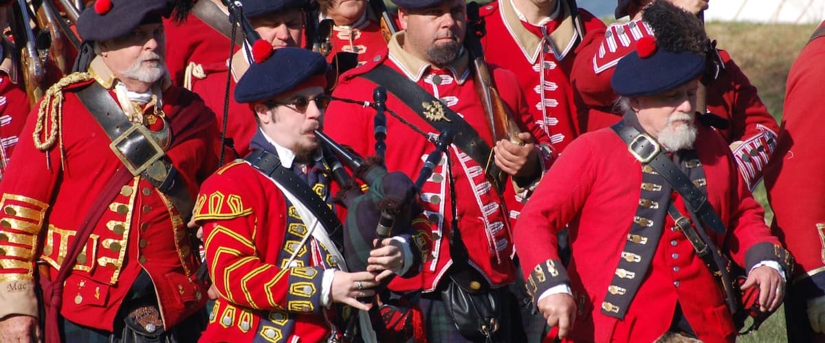 A group of men in red uniforms with gold accents, holding rifles and wearing kilts.