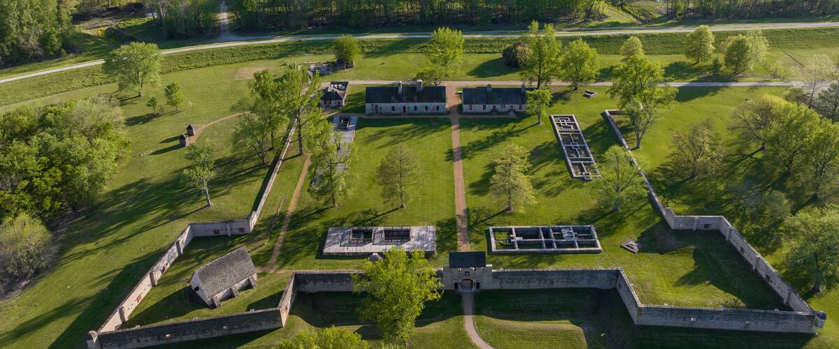 An aerial view of a historic fort with multiple buildings and a surrounding green landscape.