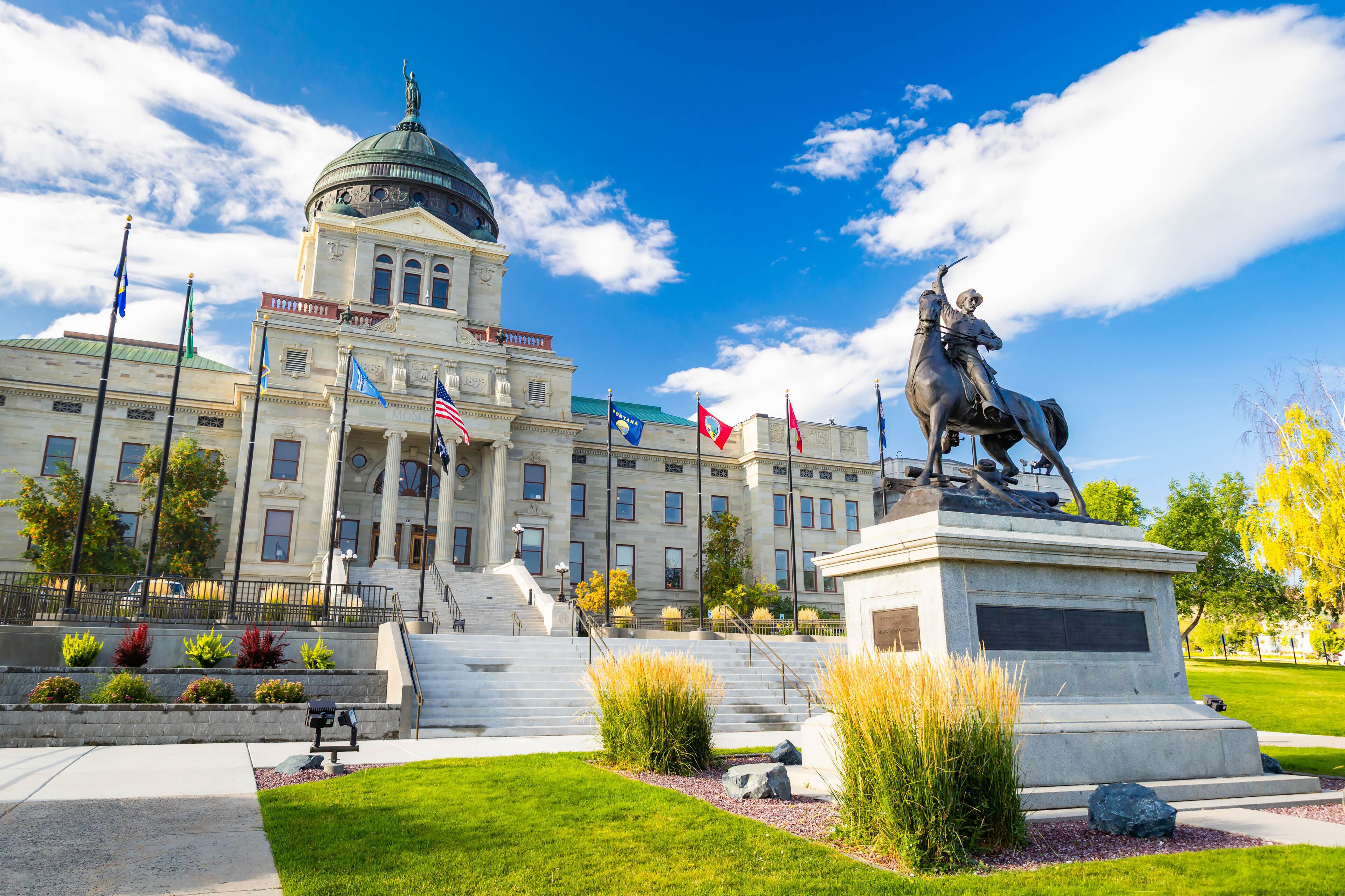 A government building with a dome, a statue of a mounted figure, and multiple flags.