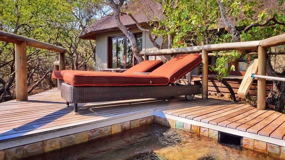 A wooden deck with a lounge chair and a small building surrounded by trees.