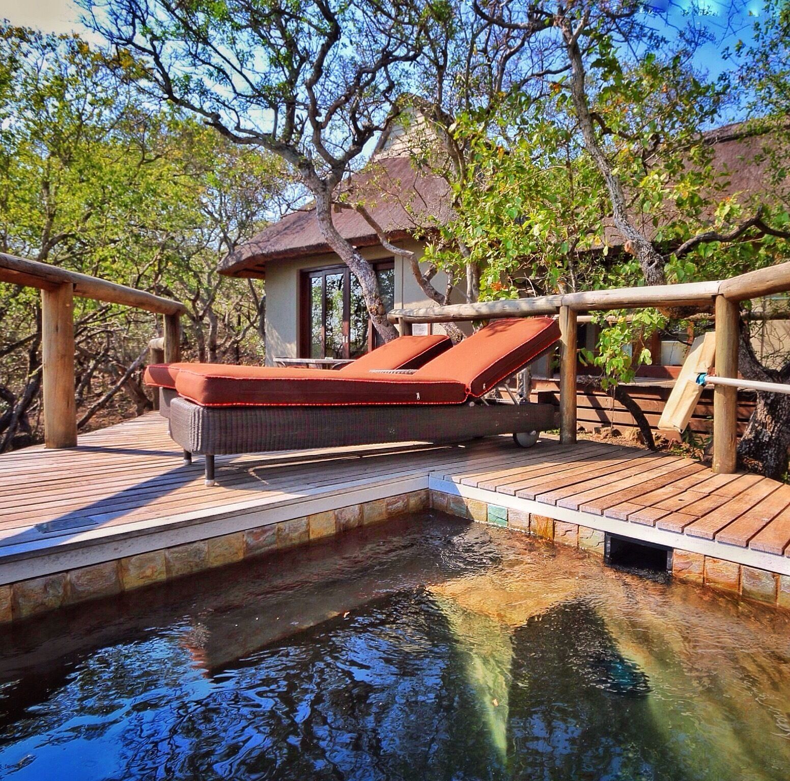 A wooden deck with a lounge chair and a small building surrounded by trees.