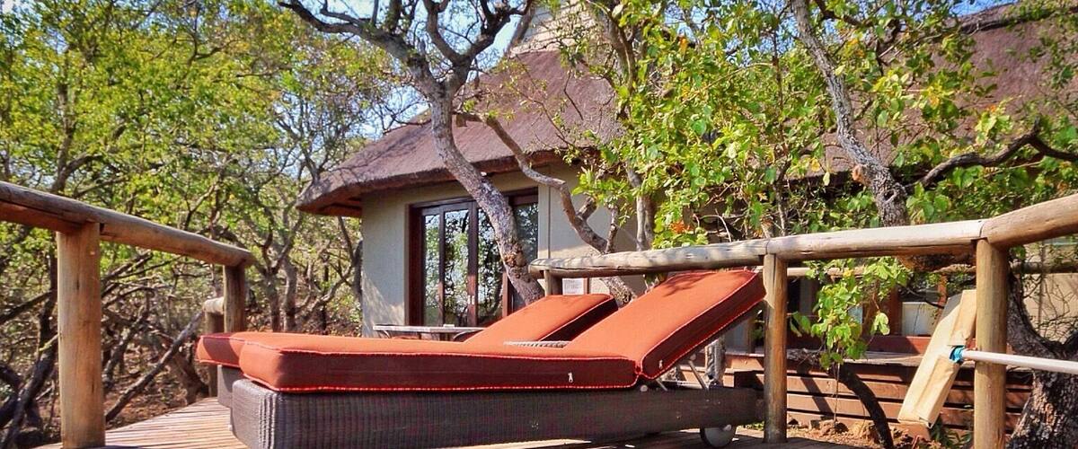 A wooden deck with a lounge chair and a small building surrounded by trees.