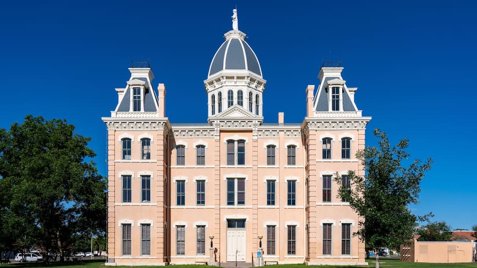 A large, historic building with a central dome and symmetrical wings, surrounded by a well-maintained lawn.