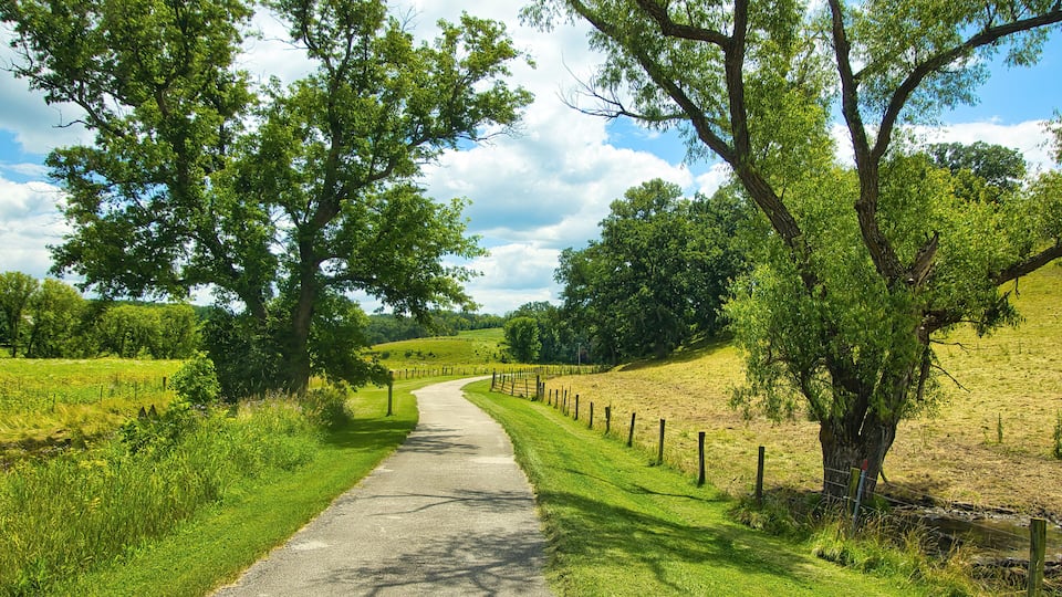 Sunny Summer day landscape of a bike trail passing trees and fenced farm fields along the Root River and Harmony-Preston Valley Trails near Preston, Minnesota.