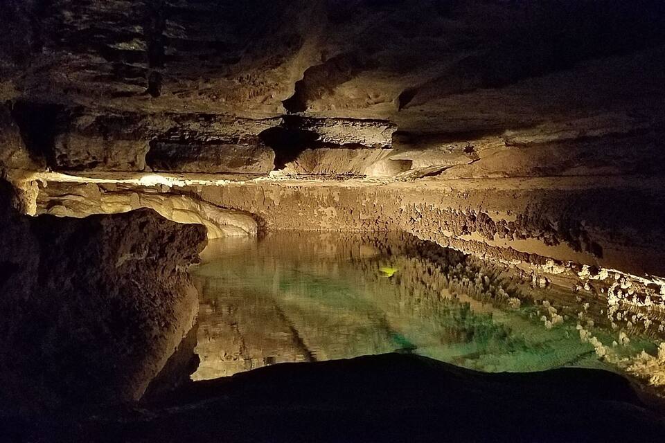 A cave with a reflective pool and illuminated walls.