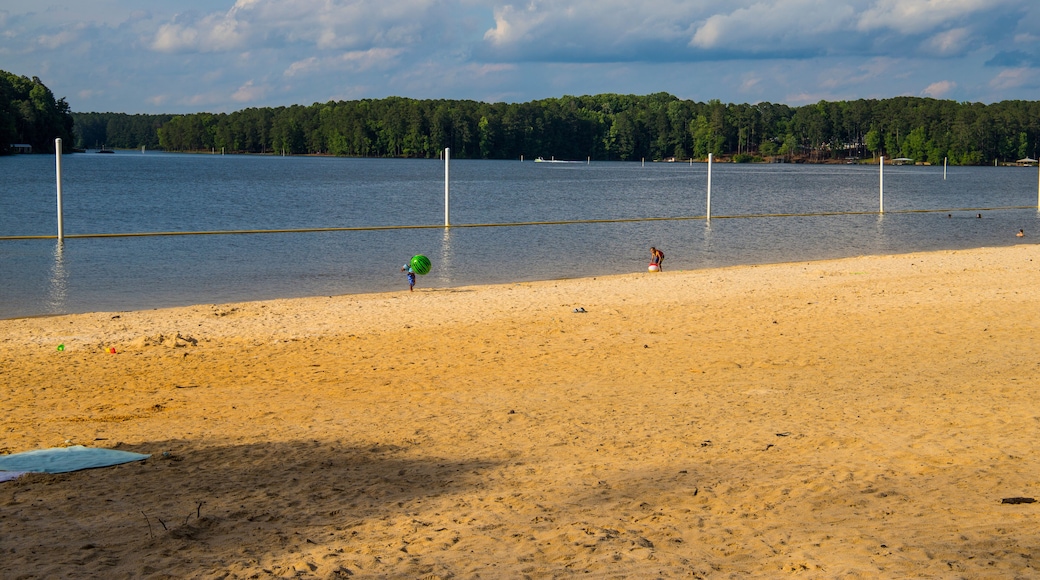 people playing in the water at the sand beach surrounded by the blue waters of Lake Acworth with lush green trees, grass and plants with blue sky and clouds at Proctor Landing Park in Acworth Georgia