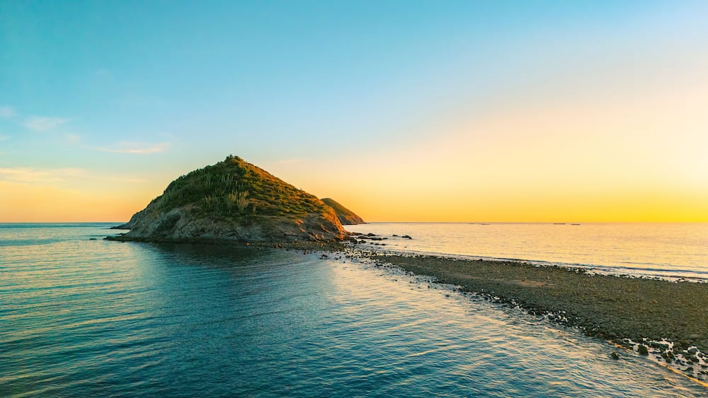 A coastal landscape with a prominent rocky island surrounded by calm sea waters.