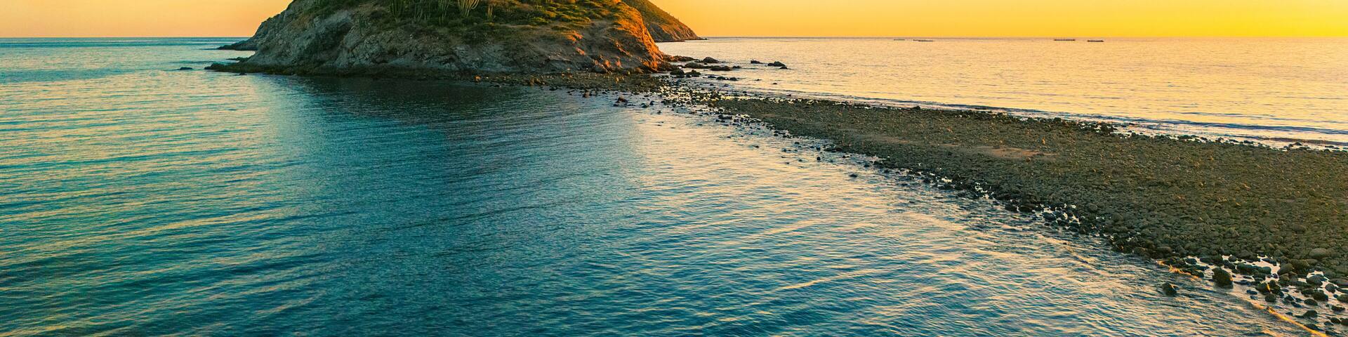 A narrow rocky road in the middle of the sea leads to San Luis Island off San Carlos Sonora, Mexico. The warm light of the sunset illuminates it. Its sahuaros create a beautiful contrasting landscape.