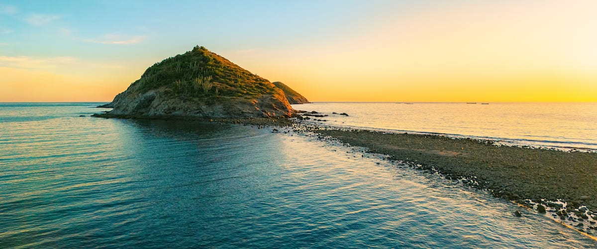 A coastal landscape with a prominent rocky island surrounded by calm sea waters.