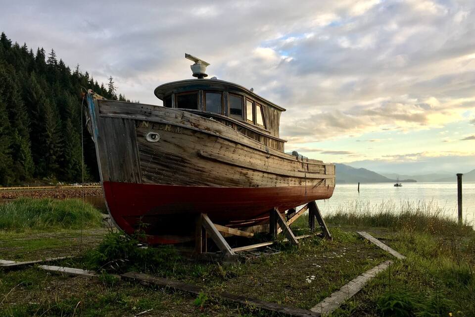 Una barca de madera en tierra, con un lago y montañas al fondo.