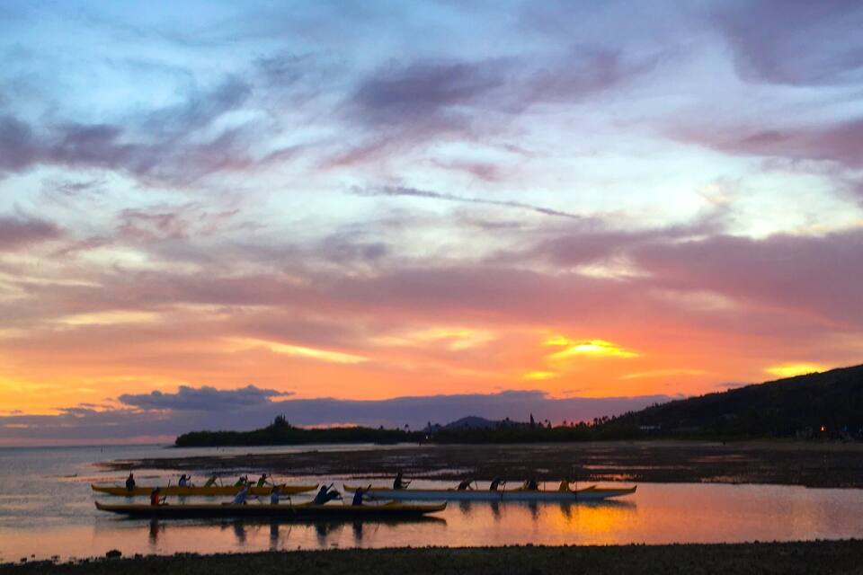 A sunset over a calm lake with several canoes on the water.