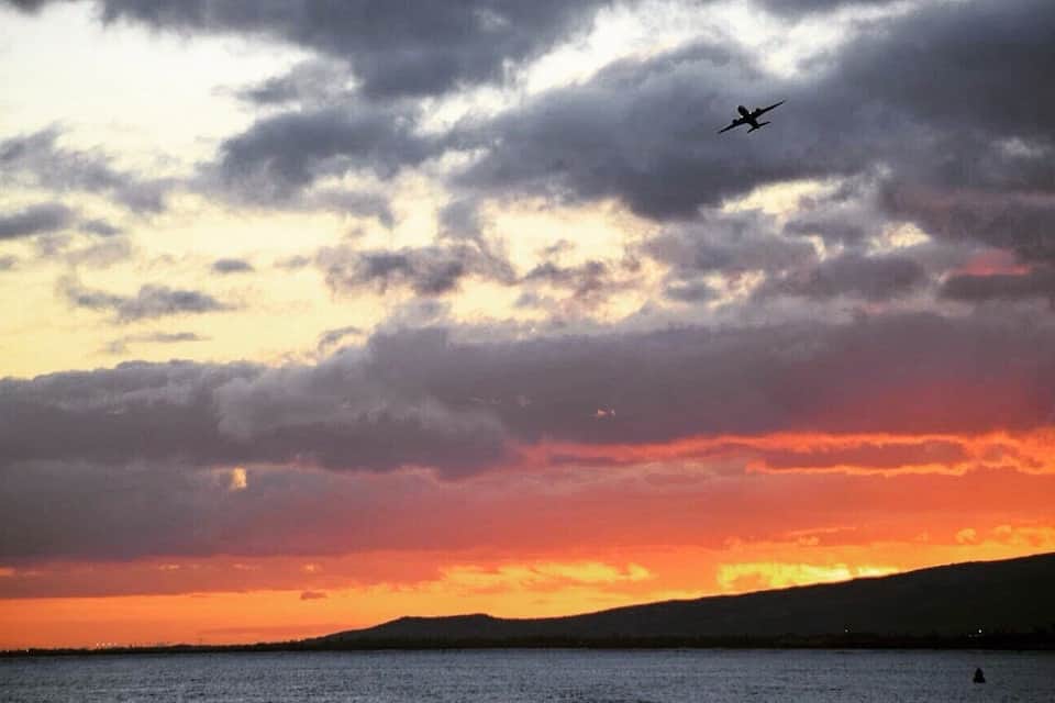 A sunset over a body of water with a silhouette of a plane flying in the sky.