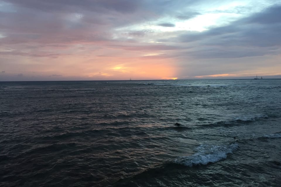 Un coucher de soleil sur une mer agitée, avec un voilier à l’horizon.
