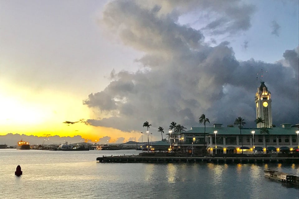 A sunset over a harbor with a clock tower and palm trees.