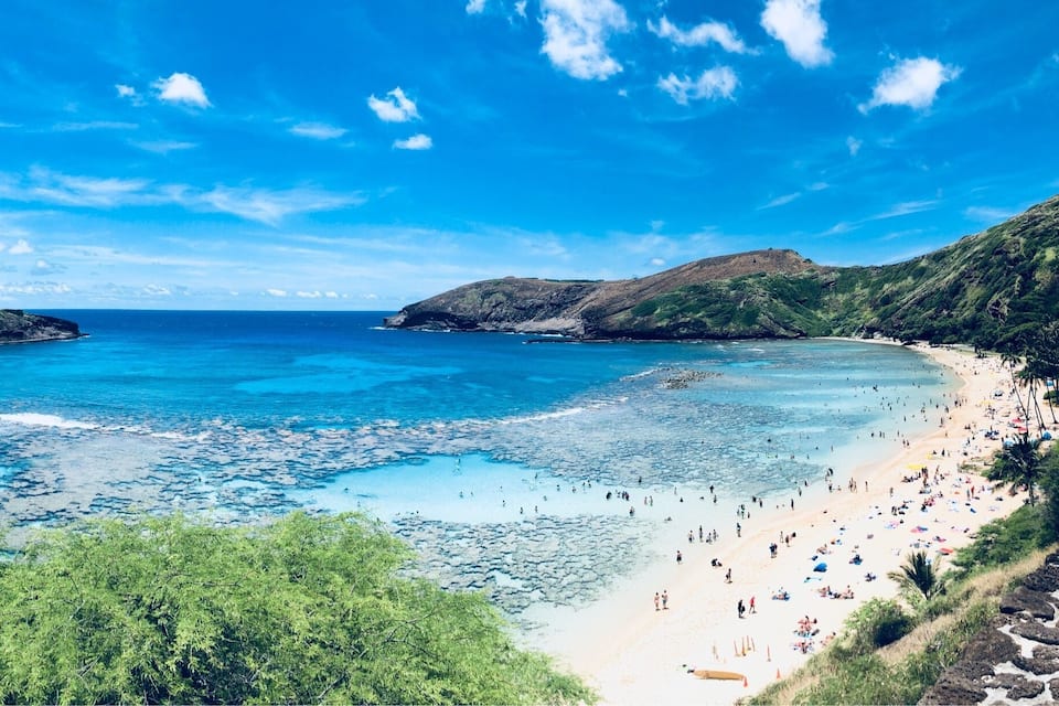 Une plage côtière aux eaux turquoise et limpides, bordée de rivages sablonneux et entourée de collines verdoyantes.