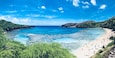 Een kuststrand met helder turquoise water, zandstranden en weelderige groene heuvels.