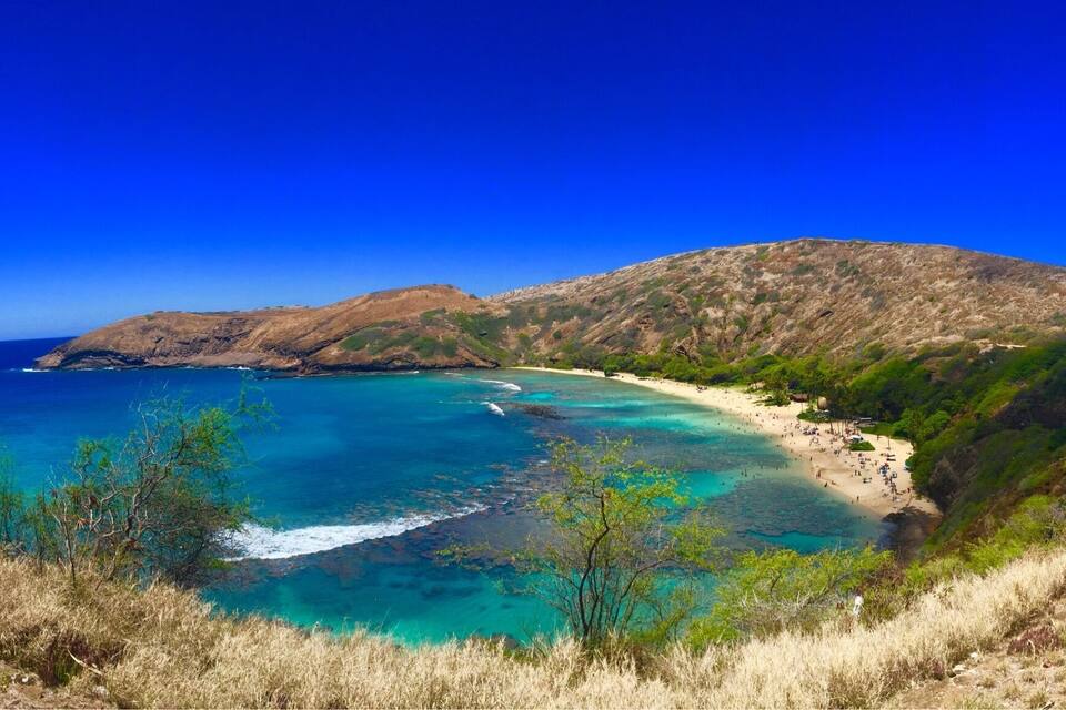 A coastal landscape with a beach, clear turquoise waters, and a mountainous backdrop.