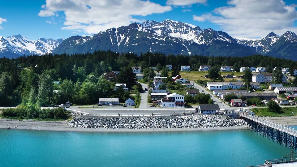 A coastal village with a pier, surrounded by mountains and clear blue waters.