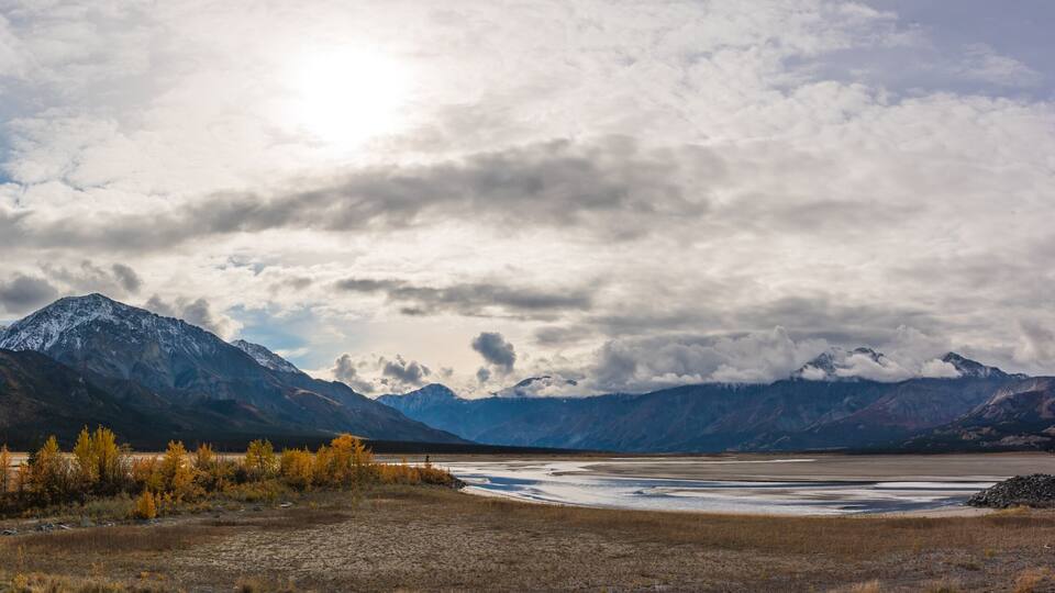 A mountainous landscape with a river and autumn-colored trees.