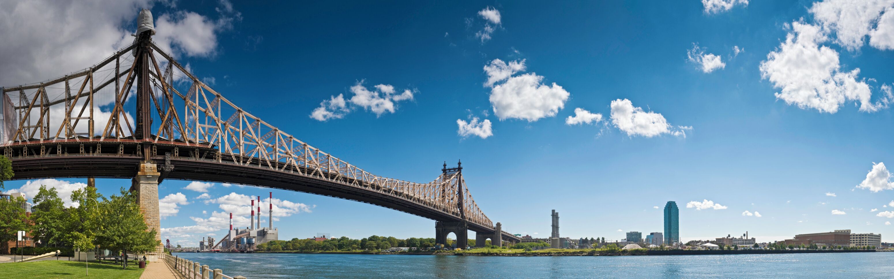A large steel bridge spanning a river, with a city skyline in the background.