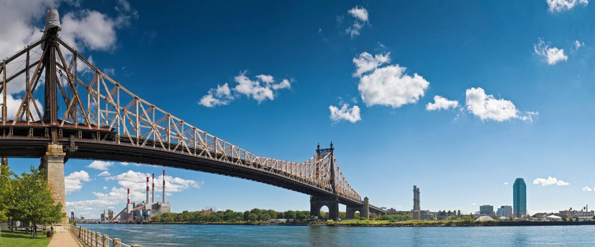 A large steel bridge spanning a river, with a city skyline in the background.