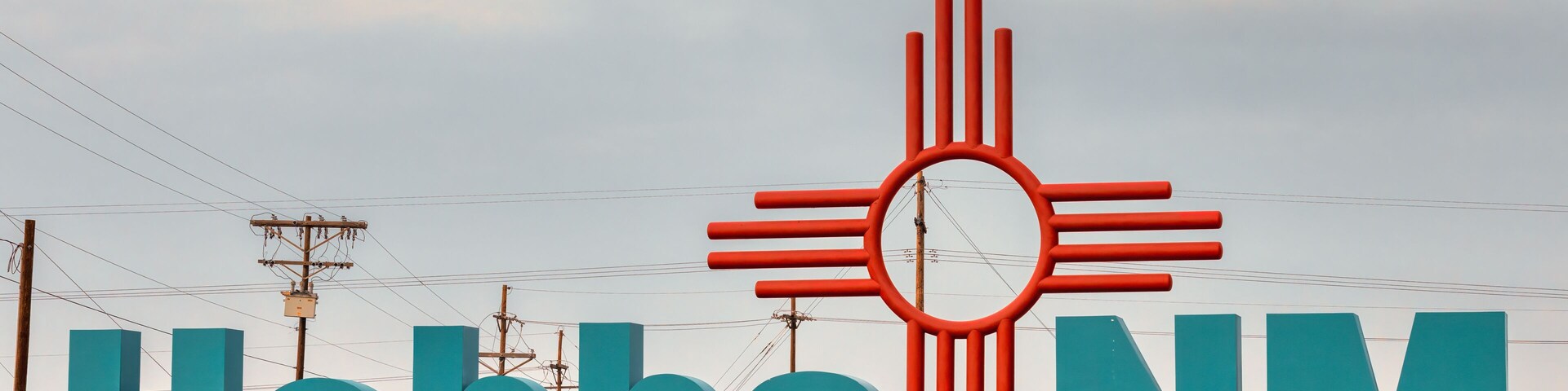 City entrance sign with large turquoise colored letters and large Zia sign