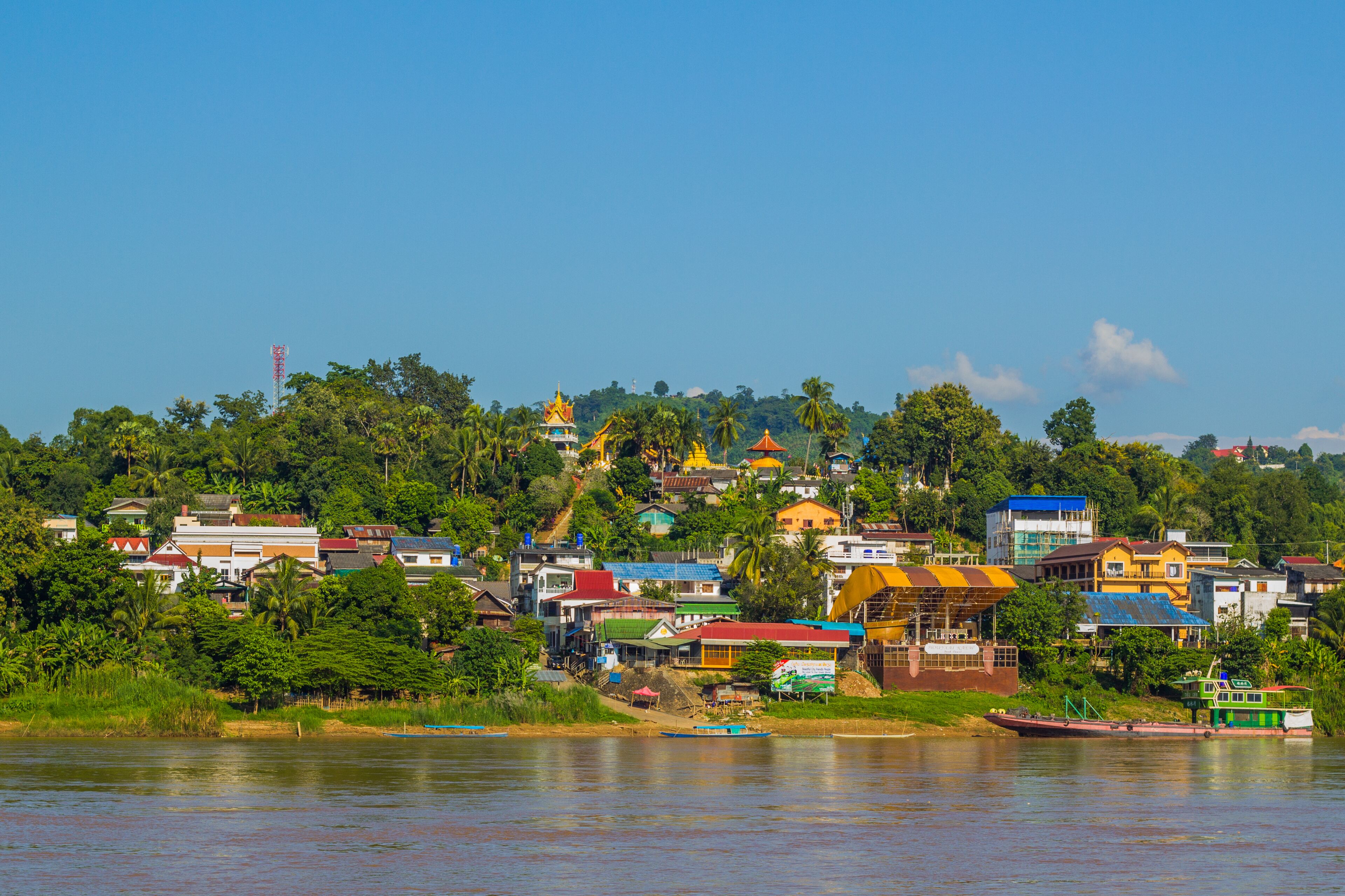 A riverside town with colorful buildings, a prominent yellow structure, and lush greenery.