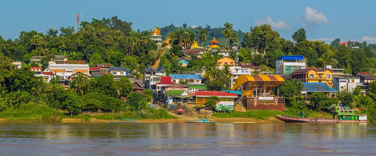 A riverside town with colorful buildings, a prominent yellow structure, and lush greenery.