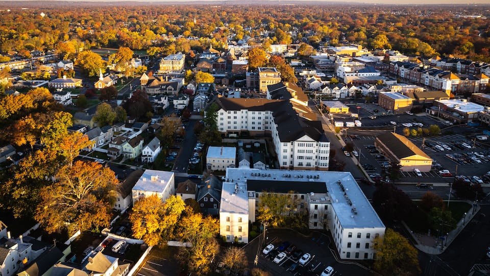 An aerial view of a town with autumn-colored trees, various buildings, and a parking lot.