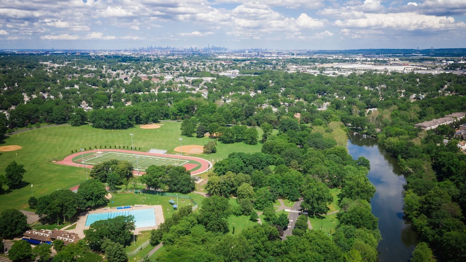 An aerial view of a park with a running track, a swimming pool, and a river.