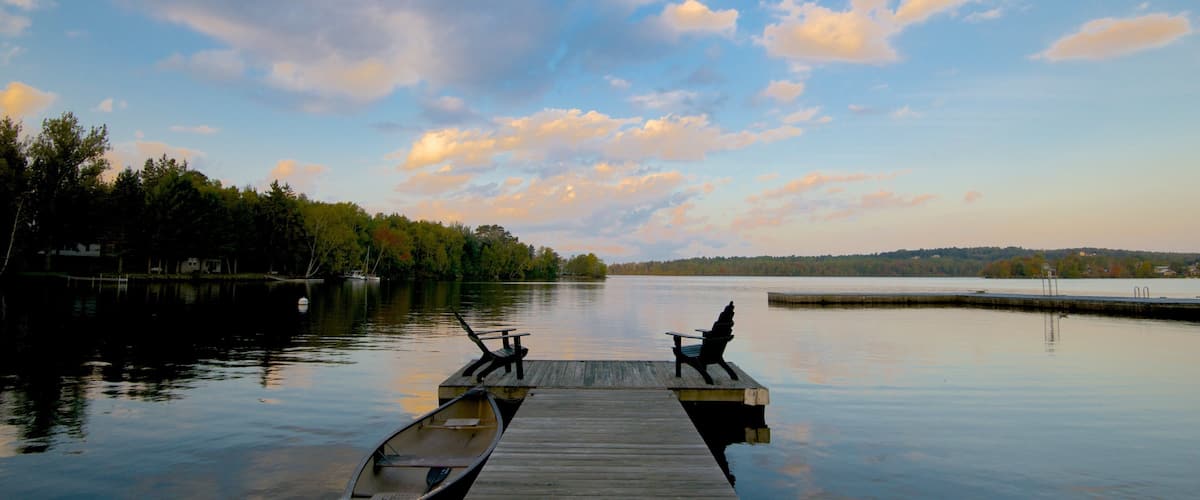 A wooden dock extending into calm waters with a backdrop of trees and a partly cloudy sky.