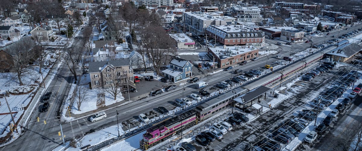 A snow-covered cityscape with a train passing through a parking lot.