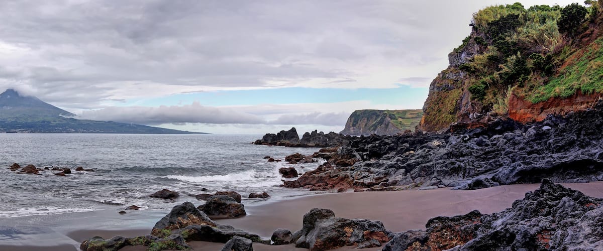 A coastal landscape with a prominent mountain, rocky shoreline, and a beach.