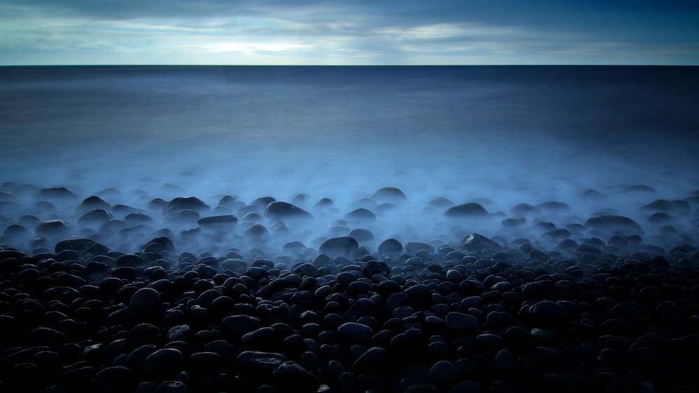 Eine felsige Küstenlinie mit einem nebligen Meer und einem bewölkten Himmel.