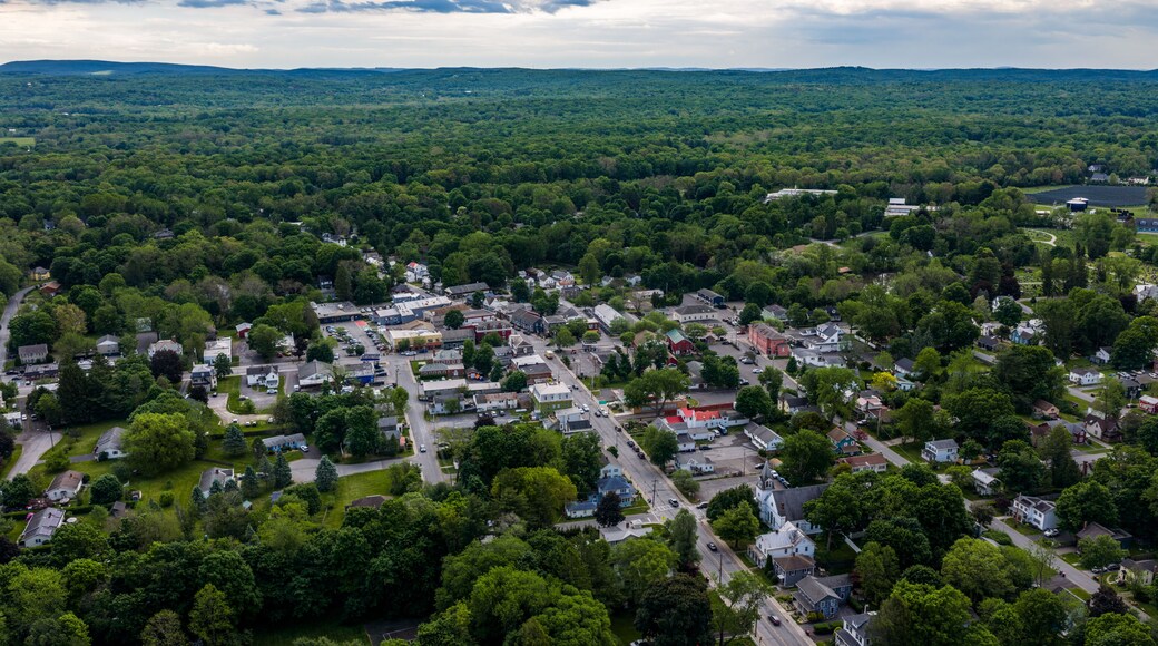 Red Hook, NY, USA - 05-20-2026 Aerial view of a small town nestled within a vast expanse of lush green forest under a partly cloudy sky.