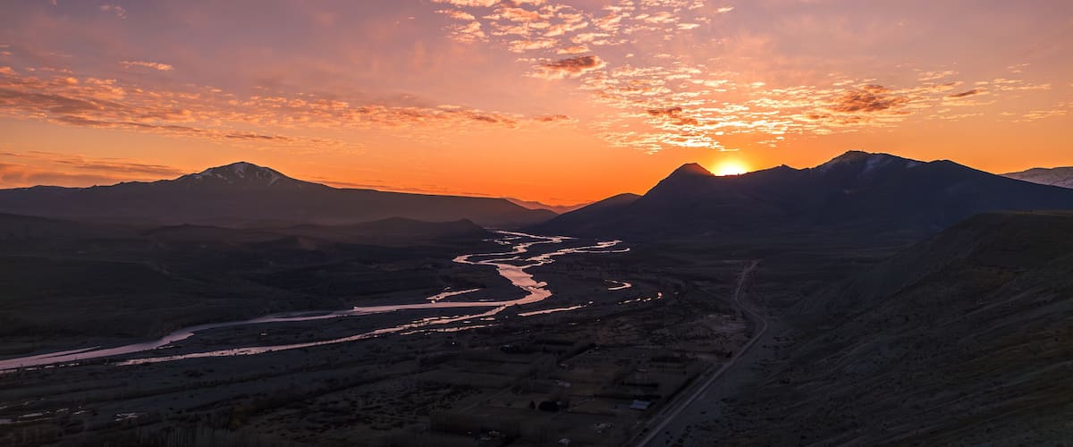 A sunset over a mountainous landscape with a winding river.