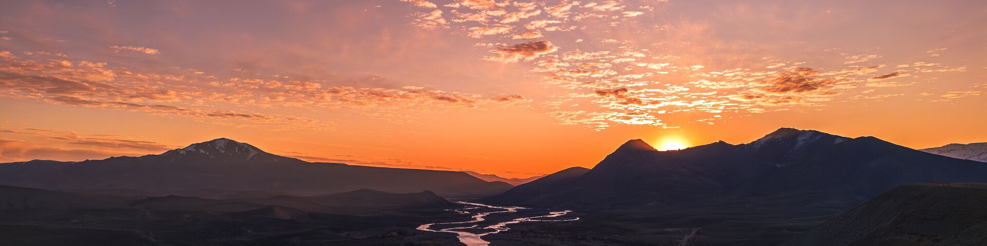 A sunset over a mountainous landscape with a winding river.