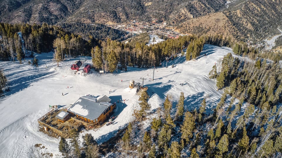 A snow-covered ski resort with a lodge, ski lifts, and forested mountains.