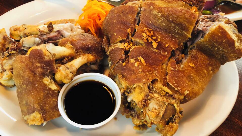 A plate of fried pork belly with a side of shredded carrots and a small bowl of sauce.