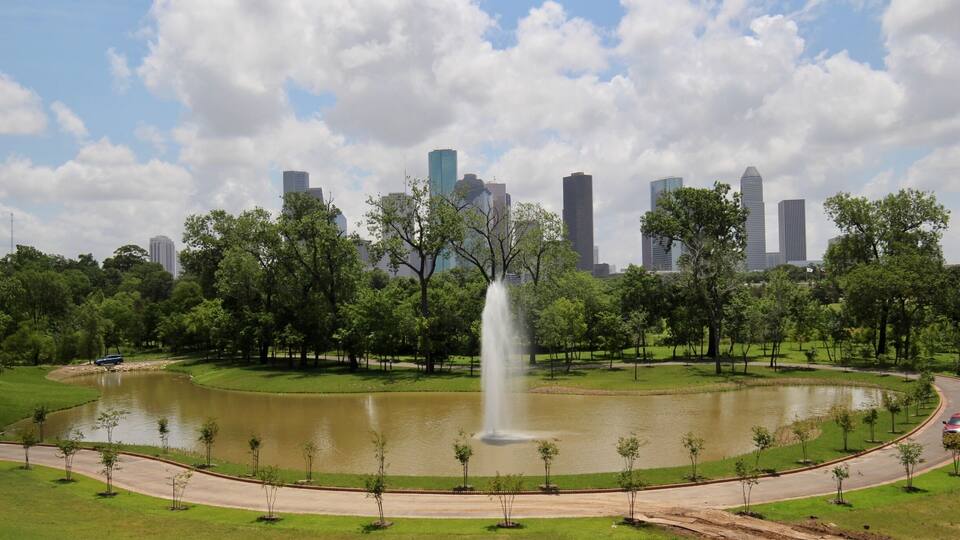 A park with a fountain, a lake, and a city skyline in the background.